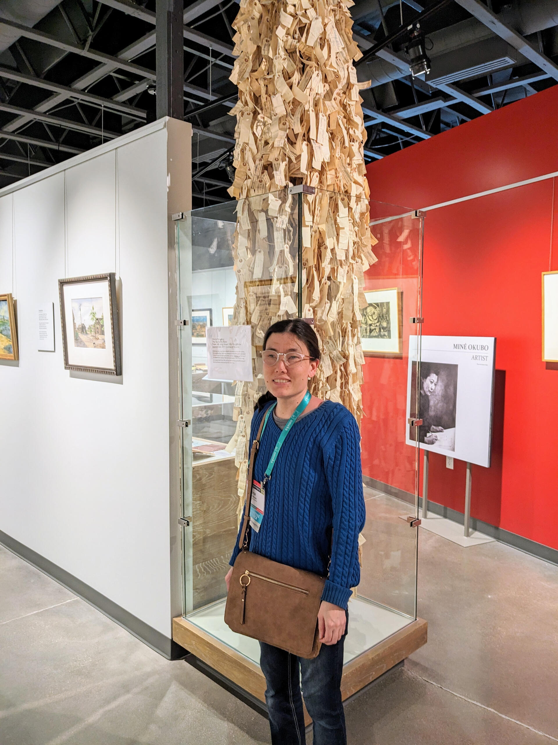 Photo of Selena Moon: Me at the Topaz Museum, the site of the Topaz incarceration camp. I am standing beside Wendy Maruyama’s “The Tag Project” display of 120,000 replica ID tags worn by Japanese Americans when they were sent to the camps during World War
